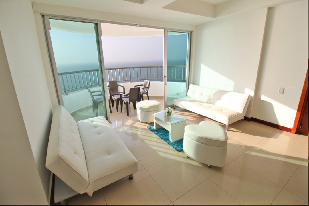 sala amoblada con sillas blancas de material cuero con un balcon en frente con vista al mar de cartagena