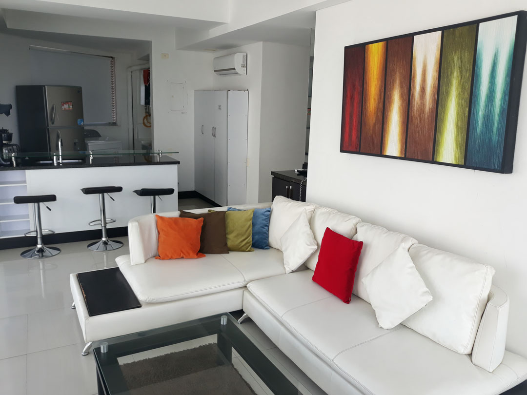 vista de apartamento con sala de estar amoblada con sofá en L y cocina abierta con barra y butacas para 3 personas