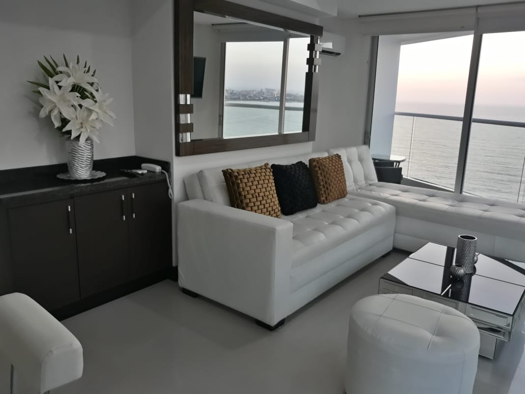 sala de estar de estilo elegante con muebles en cuero blanco y mesa de café, un ventanal da salida al balcón con vista al mar