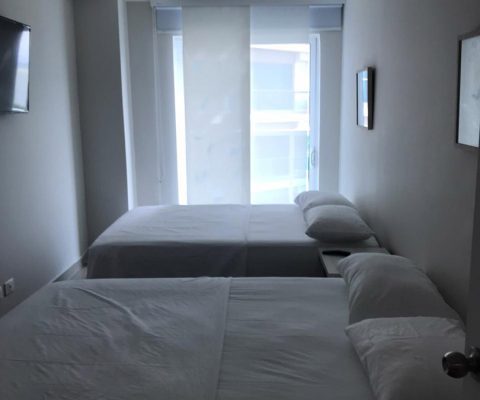 habitación equipada con 2 camas dobles, nochero y tv en pared, su ventana de piso a techo con cortina estilo panel japonés
