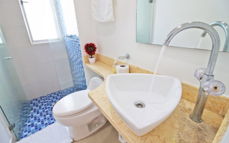 baño de estilo moderno con lavamanos triangular de sobreponer, hay un sanitario tradicional y ducha enchapada en color azul