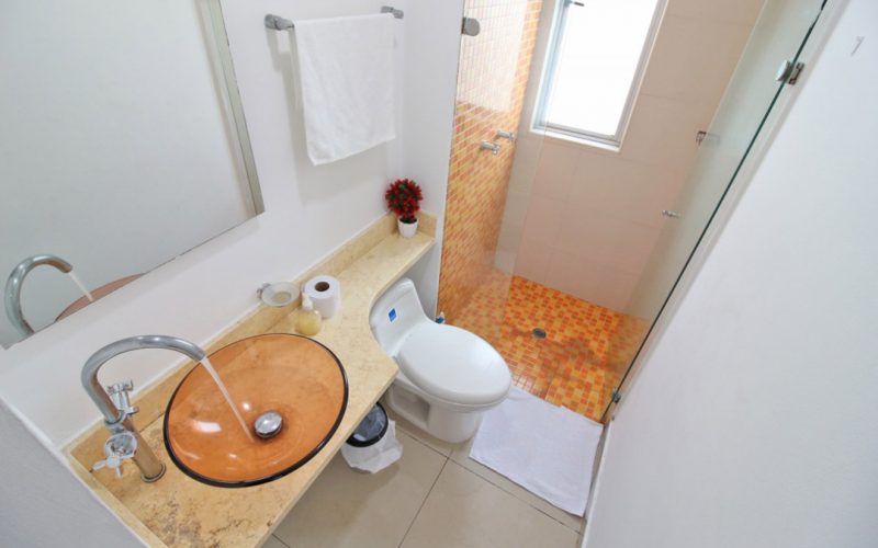 baño con lavamanos en vidrio y estilo de sobreponer, sanitario y ducha enchapada en azulejos color naranja