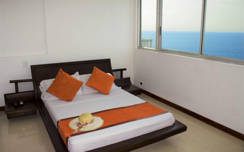 Habitación con cama doble café con cobertor naranja y ventana con vista al mar de Cartagena