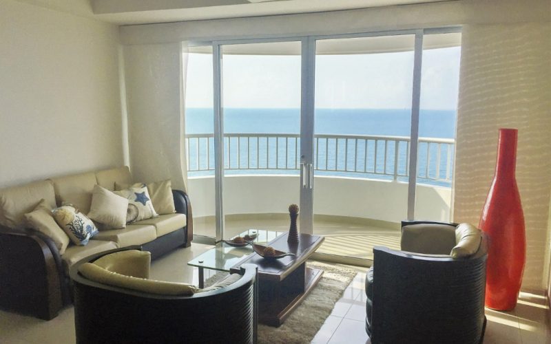 sala amoblada con sillas beige con cafe frente a balcon con vista a la playa de bocagrande