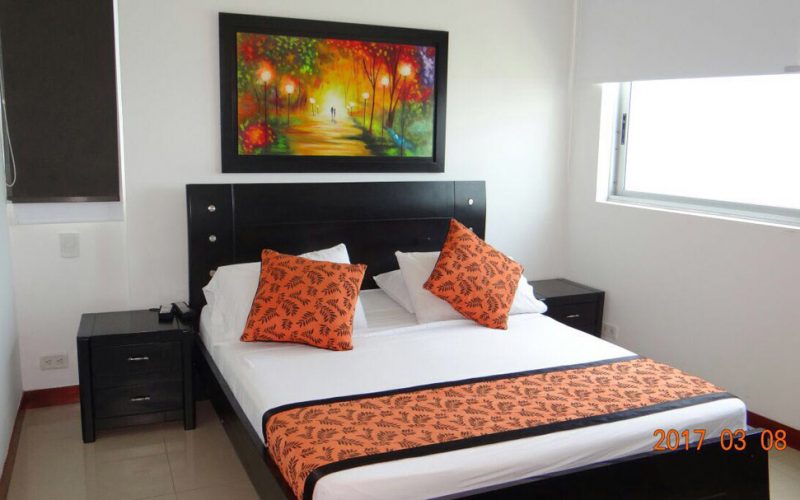 habitacion con cama doble en madera negra con sabanas blancas cobertor naranja y dos mesas de noche negras
