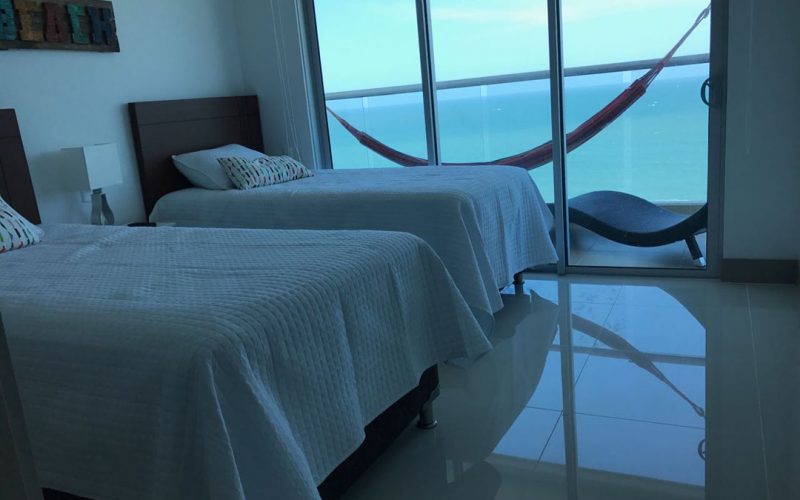 habitacion con dos camas sencillas en madera oscura y balcon vista al mar con hamaca de colores