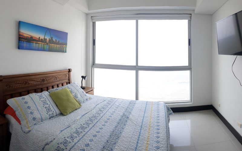 habitación con cama doble de estilo tradicional nochero, tv en pared y ventanal piso techo que da vista al mar de Cartagena