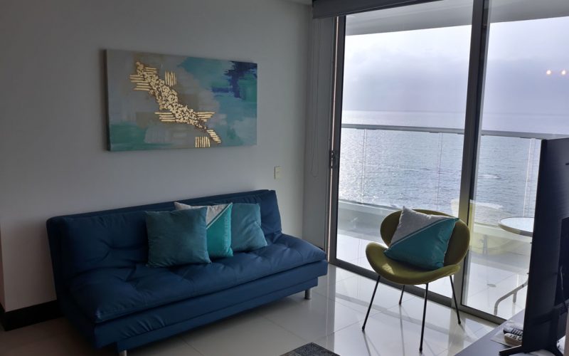sala de estar con sofá y silla de estilo moderno. una puerta ventana da salida a un balcón con vista al mar de Cartagena