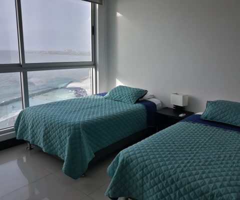 habitación de apartamento equipado con dos camas sencillas y nochero, su ventana da vista a la paya de Bocagrande Cartagena