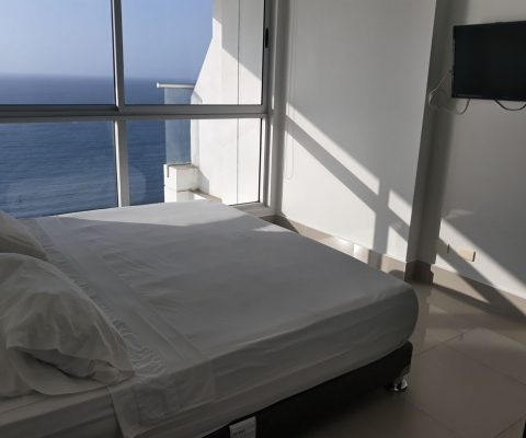 habitación con cama doble y tv plana, el ventanal piso a techo da una vista privilegiada sobre el mar de Cartagena