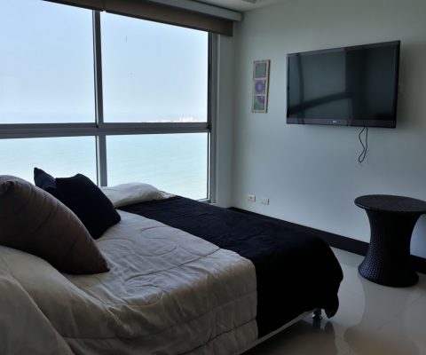 habitación con cama doble, mesa auxiliar y tv, el ventanal piso a techo da vista sobre el mar de Cartagena