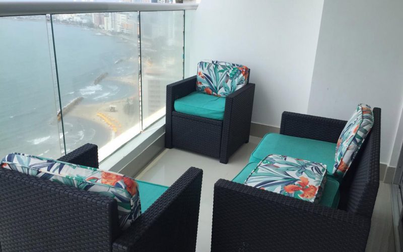 balcón amoblado con sillas coloridas, sofá y 2 poltronas; que ofrece una vista total de la playa de Bocagrande en Cartagena