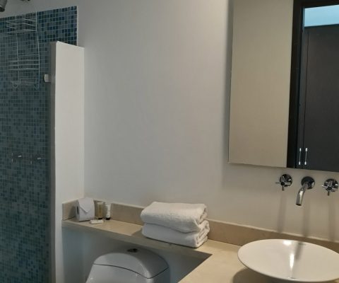 baño con lavamanos de porcelana, grifería moderna, sanitario, encimera de piedra y ducha con detalle de enchape azul